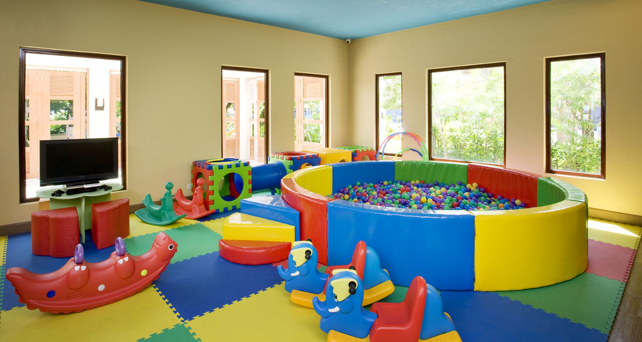 Un espace de jeux avec des structures colorées, une piscine à balles et un téléviseur posé sur un meuble.
