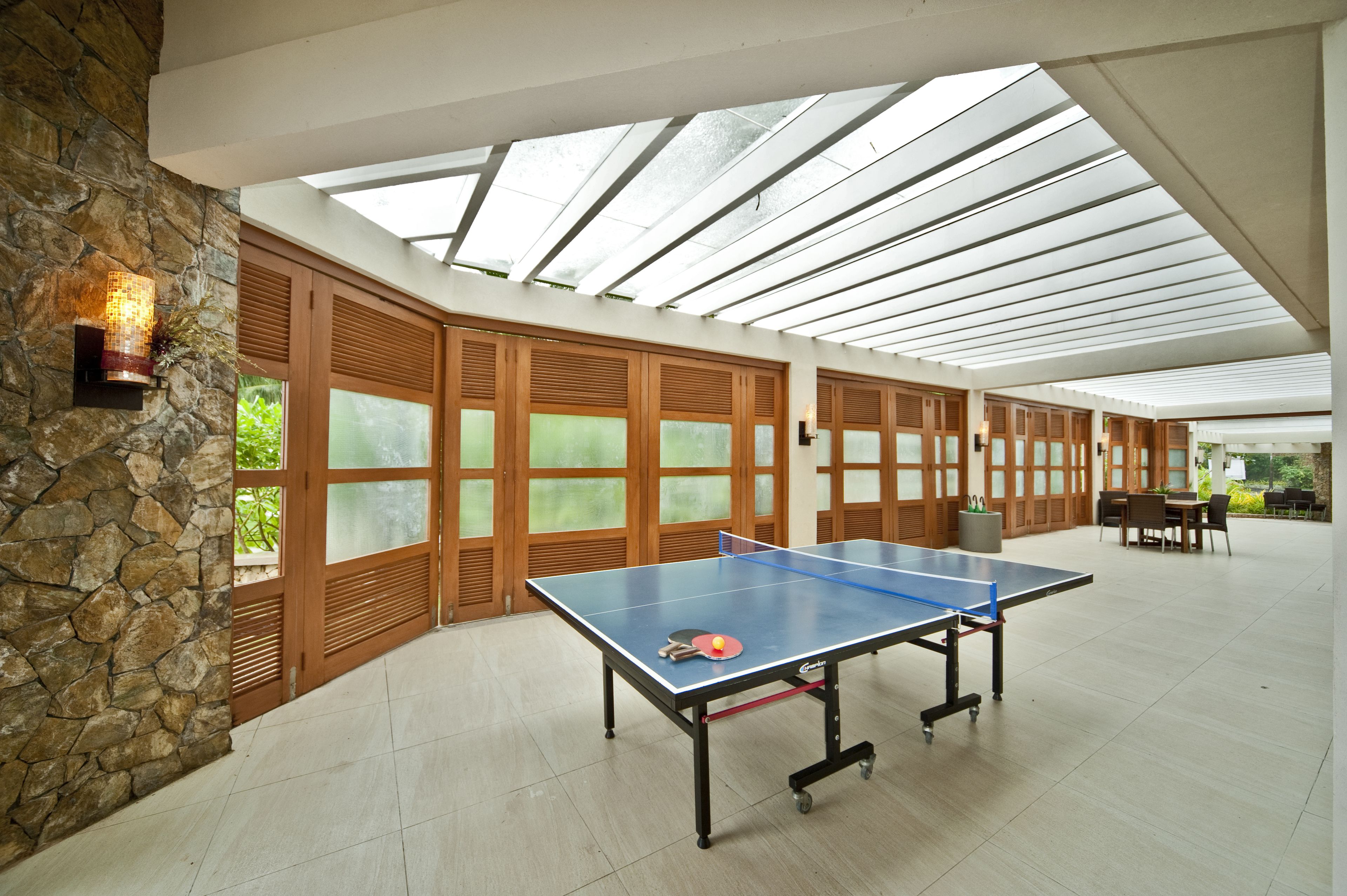 Amplio espacio interior con mesa de ping pong, paredes de piedra y grandes ventanales que dejan entrar luz natural.