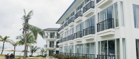 Un hotel de varios pisos con balcones, zona de piscina y jardines tropicales.