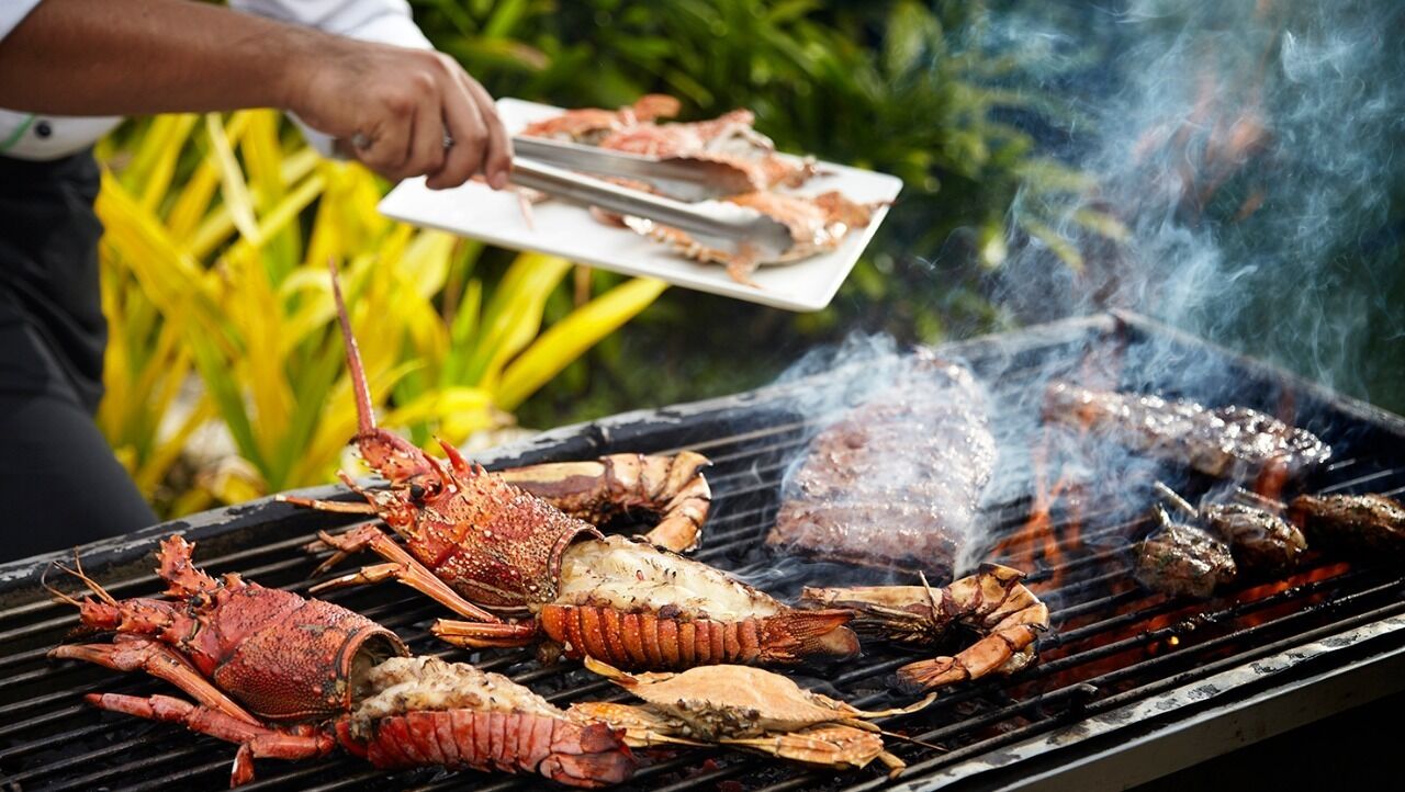 En grill med forskelligt fisk og skaldyr, herunder hummer og rejer, tilberedes udendørs.
