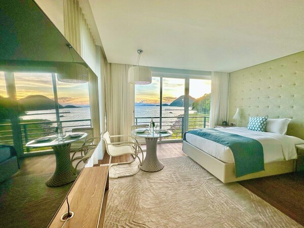 Habitación de hotel moderna con una cama grande, una mesa de comedor y vistas al mar.