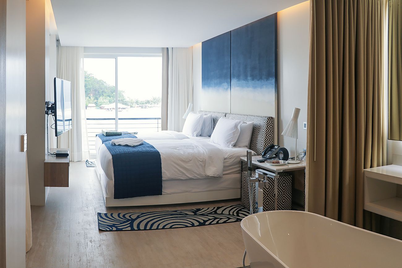 Habitación de hotel moderna con una cama grande, una bañera, un escritorio con lámpara y vistas al exterior.