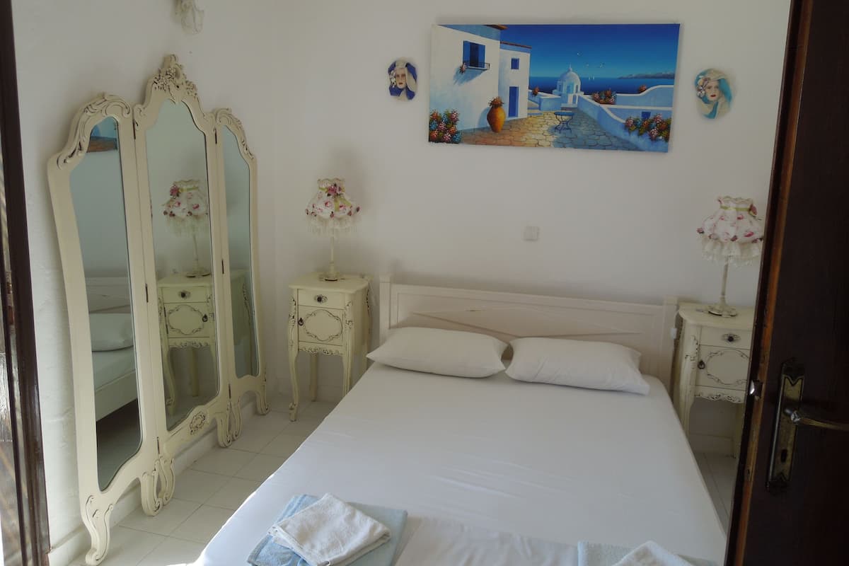 A bedroom with a bed, two nightstands, two mirrors, and a painting of a coastal scene.