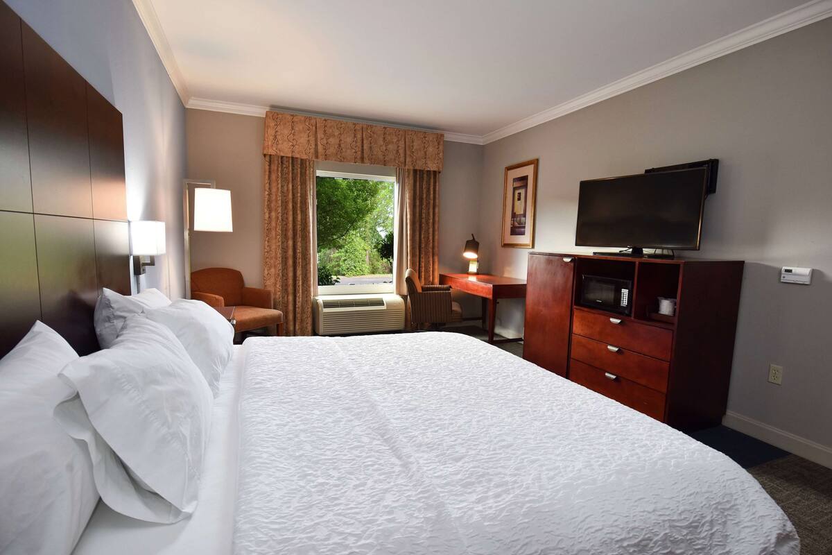 A hotel room with a large bed, a desk with a chair, a television, and a window with curtains.