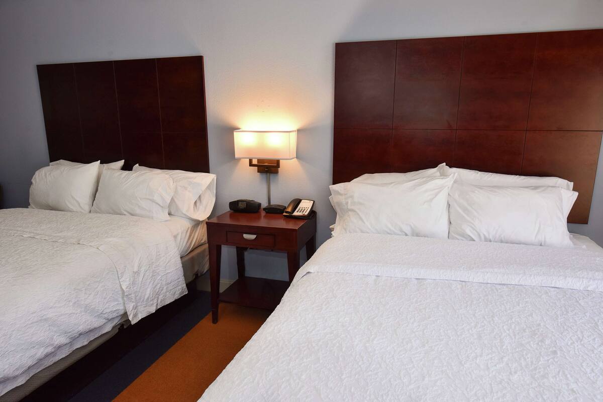 A hotel room with two beds, a bedside table with a lamp, and a telephone.