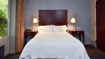 A neatly made bed with white linens, two bedside lamps, and a dark headboard in a room with a window and a door.