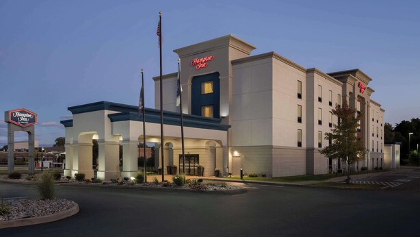 A Hampton Inn hotel with a modern design, featuring a prominent entrance, flagpole, and well-lit exterior.