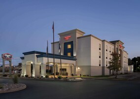 Un hotel Hampton Inn con diseño moderno, que presenta una entrada destacada, asta de bandera y fachada bien iluminada.