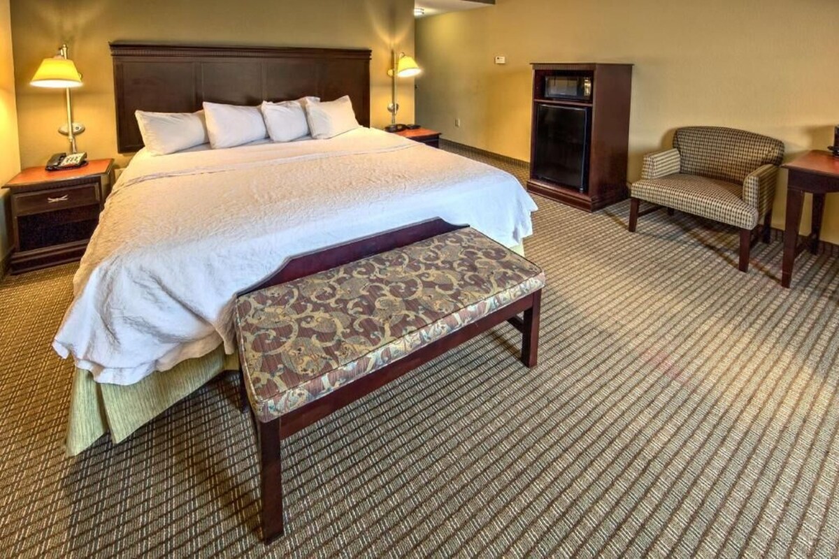 Una habitación de hotel con una cama grande, un banco, una silla, un escritorio y un televisor.