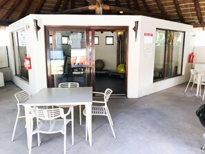 A covered outdoor area with a table and chairs, a fire extinguisher, and a door leading to an interior space. - Sunshine Letting Apartments (Cape Town)