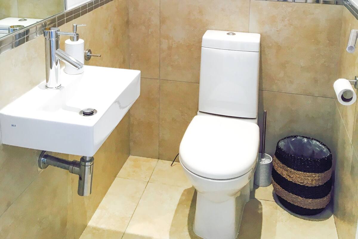 Une salle de bain avec des toilettes, un lavabo et une poubelle. Des reproductions botaniques encadrées ornent le mur.