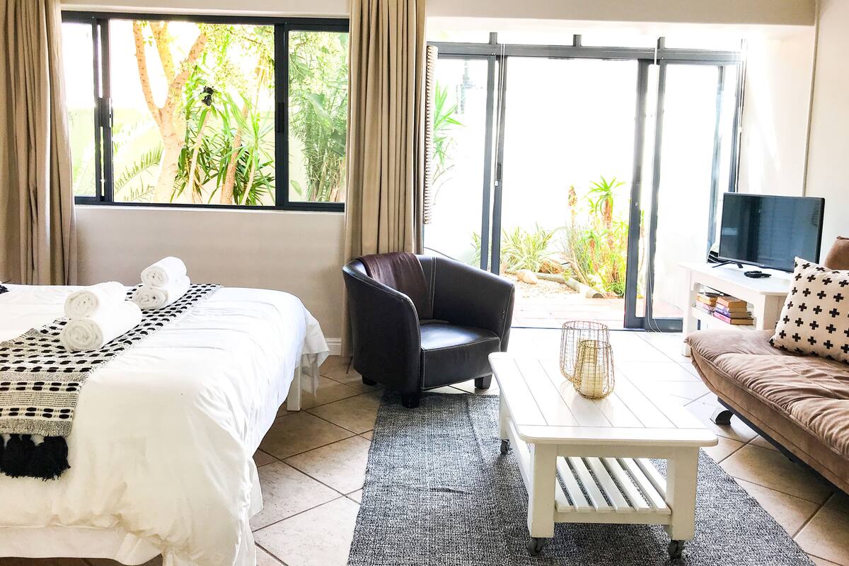 Une chambre d’hôtel avec un lit, un fauteuil en cuir noir, une table basse blanche, un canapé marron et un téléviseur.