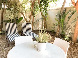 A patio with two striped lounge chairs, a white table, and a potted plant. - Sunshine Letting Apartments (Cape Town)