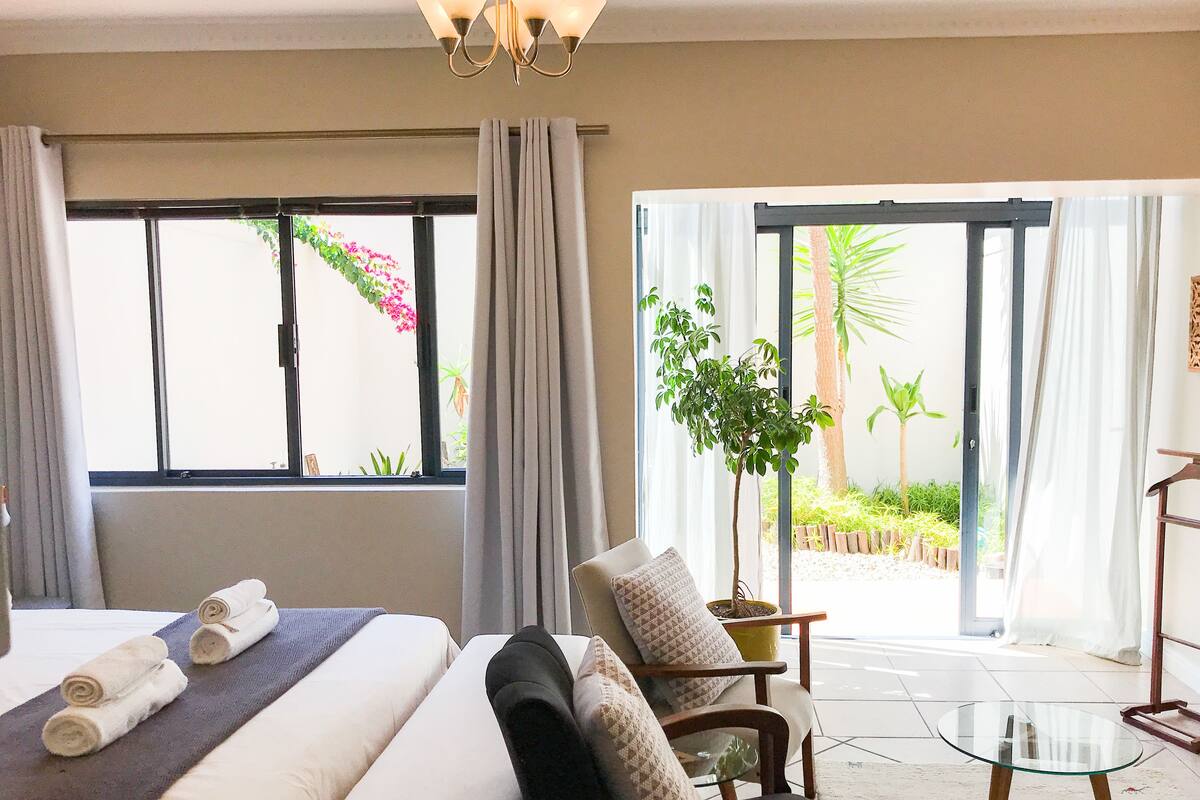 Une chambre d’hôtel avec un lit, une chaise, une petite table et une vue sur un jardin, accessible par une porte coulissante.
