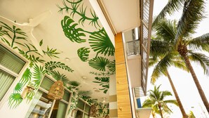 A hotel interior with a ceiling decorated with tropical leaf patterns, a modern staircase, and a view of palm trees outside. - The Local House (Miami Beach)