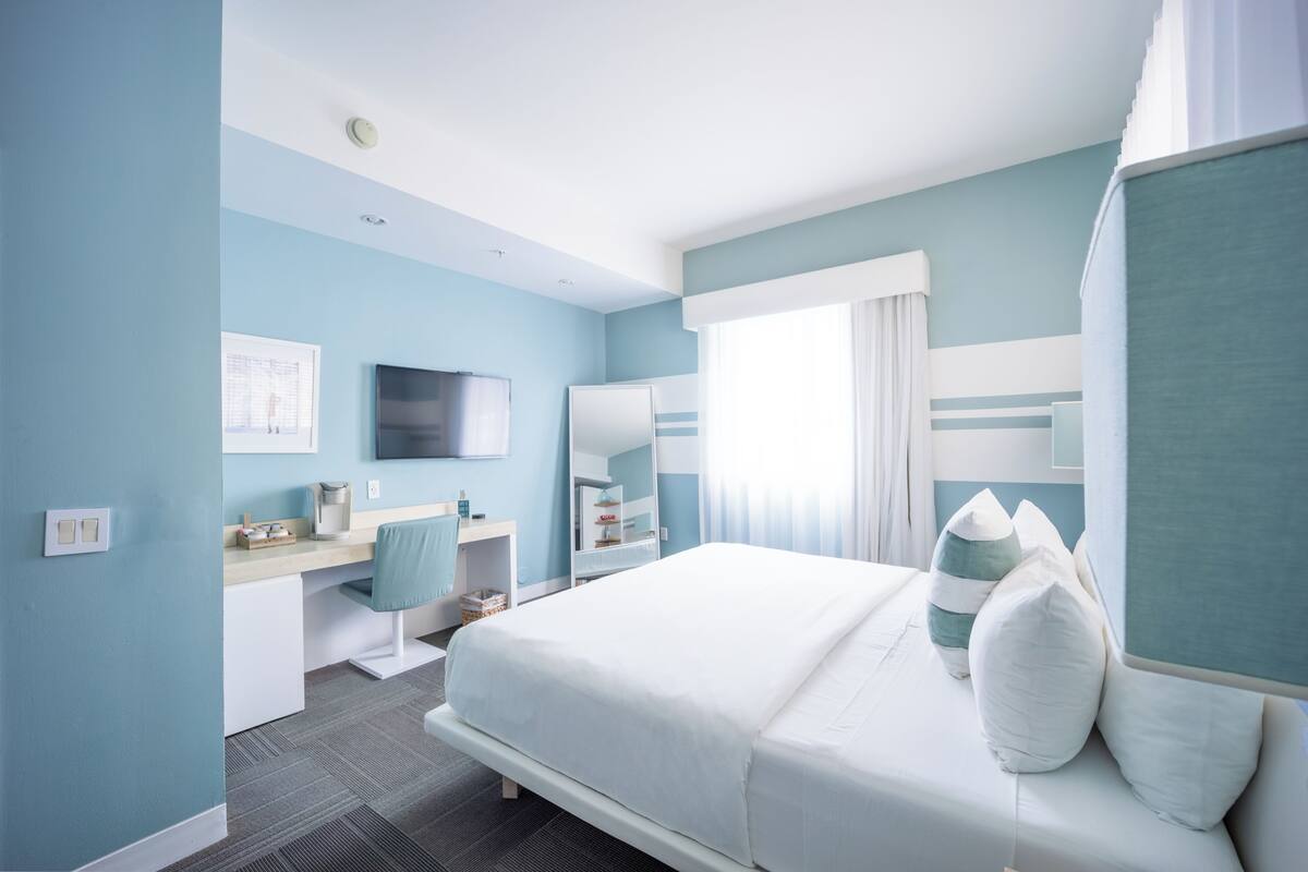 Une chambre d’hôtel avec un lit, un bureau, une télévision et une fenêtre avec des rideaux.