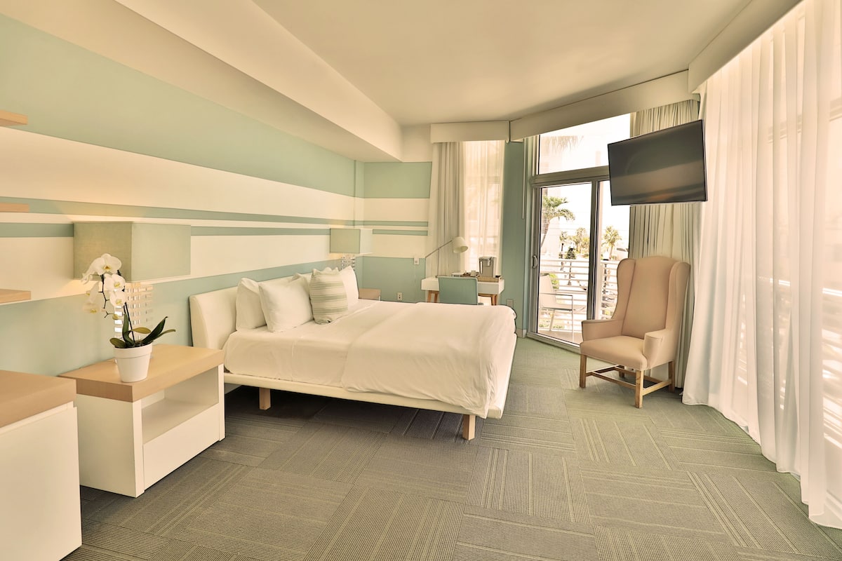 Une chambre d’hôtel avec un lit, une chaise, une télévision et une fenêtre avec des rideaux.