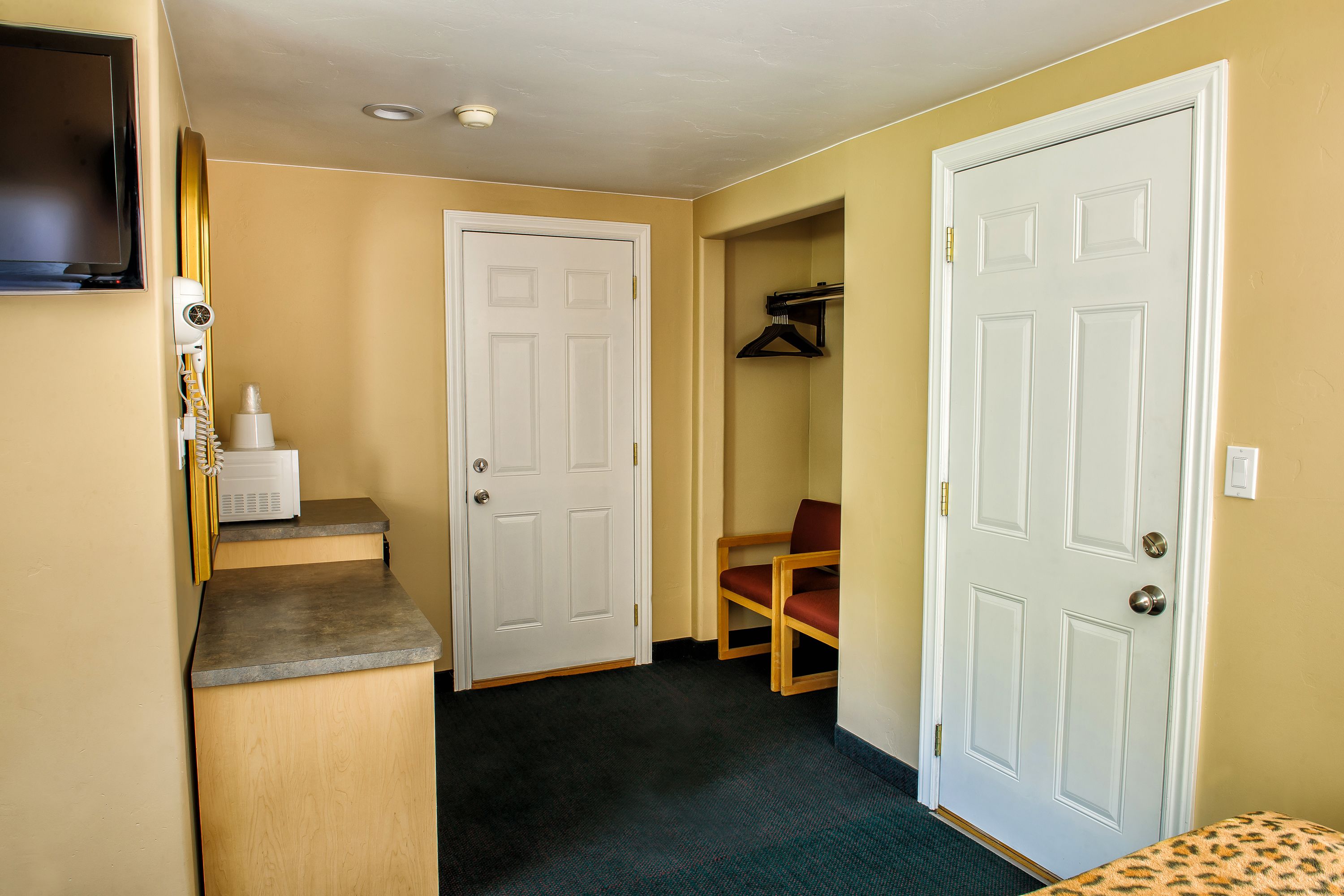 A hallway with a microwave on a counter, a chair, and two doors.