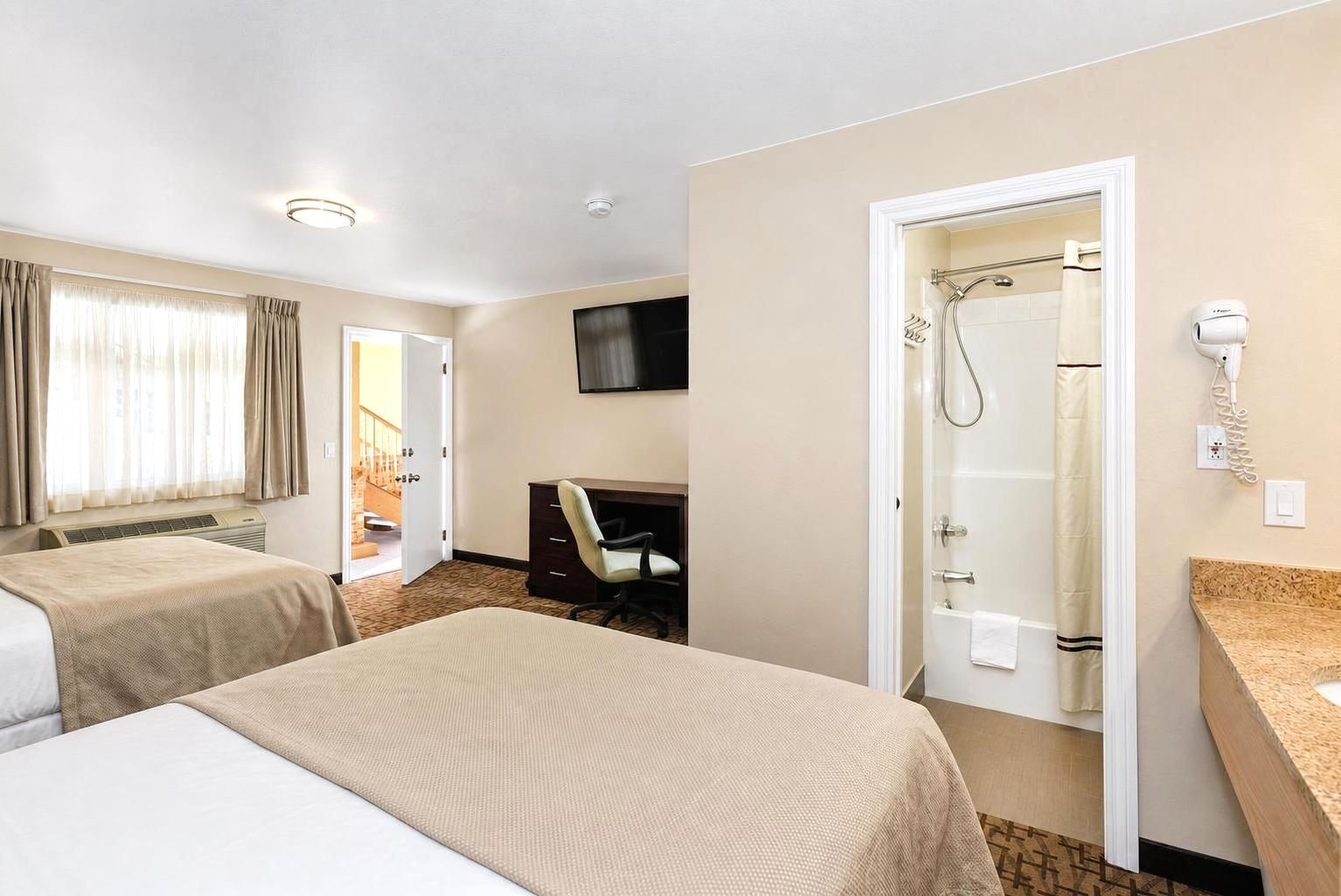 A hotel room with two beds, a desk, a TV, a shower, and a hairdryer.