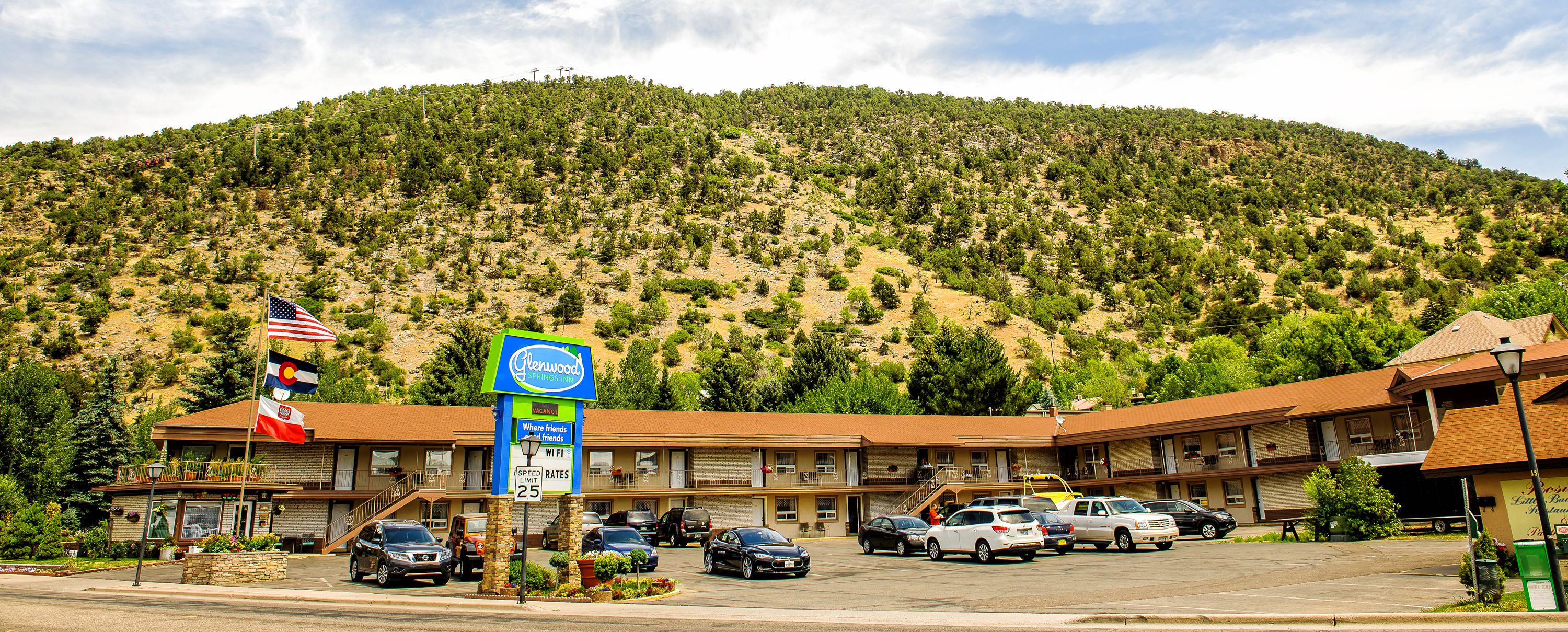 Un motel situé au pied d’une montagne, doté de nombreux espaces de stationnement et orné de drapeaux.