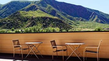 Una terraza con tres sillas de metal y una mesa redonda pequeña, con vistas a un paisaje montañoso.