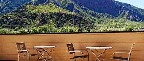 Eine Terrasse mit drei Metallstühlen und einem kleinen runden Tisch, mit Blick auf eine Berglandschaft.