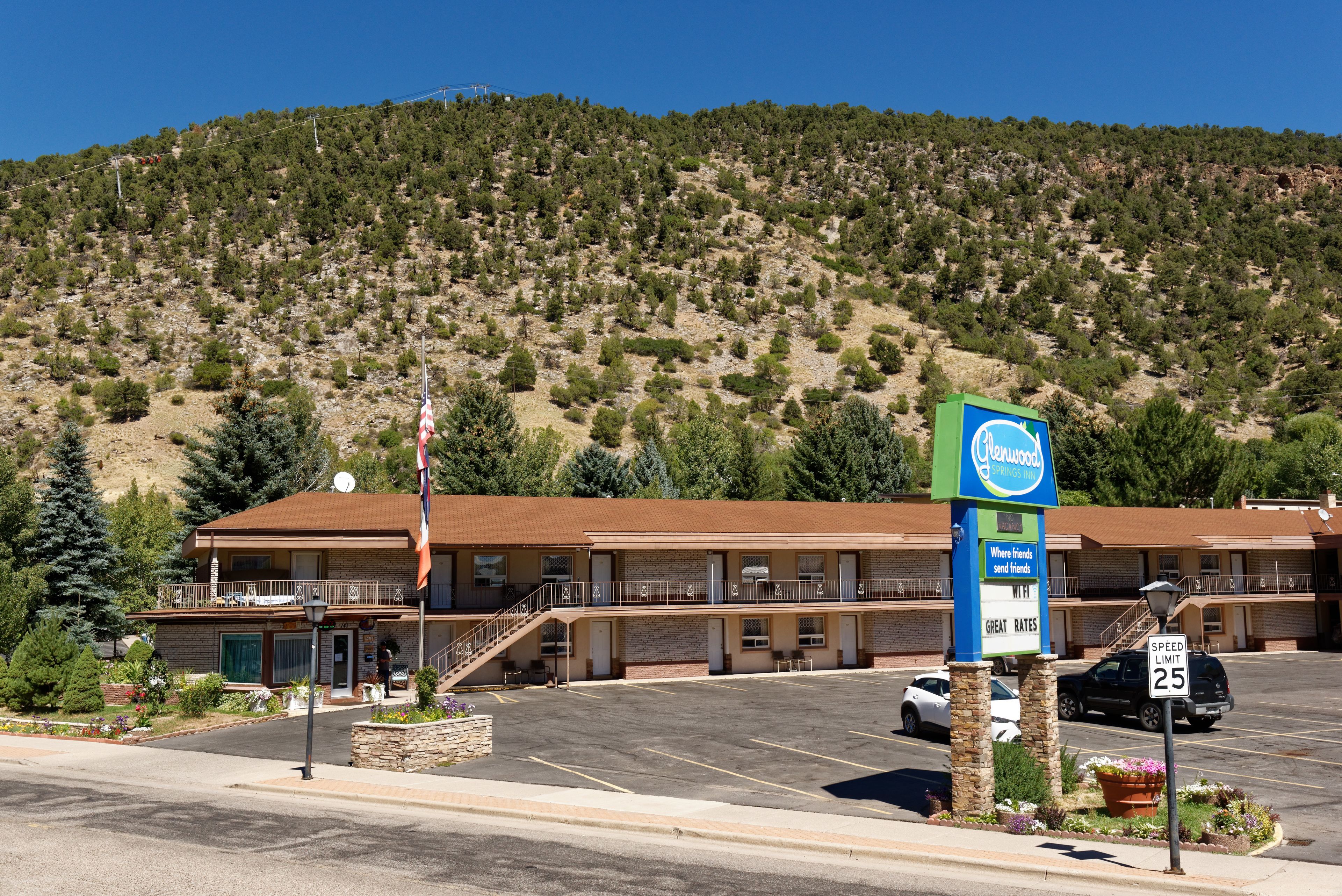 A motel with a parking lot, a speed limit sign, and a mountainous backdrop.