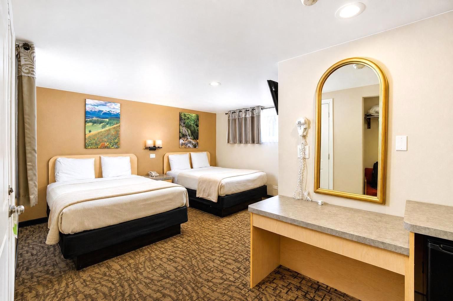 A hotel room with two beds, a large mirror, a desk, and a small bathroom.