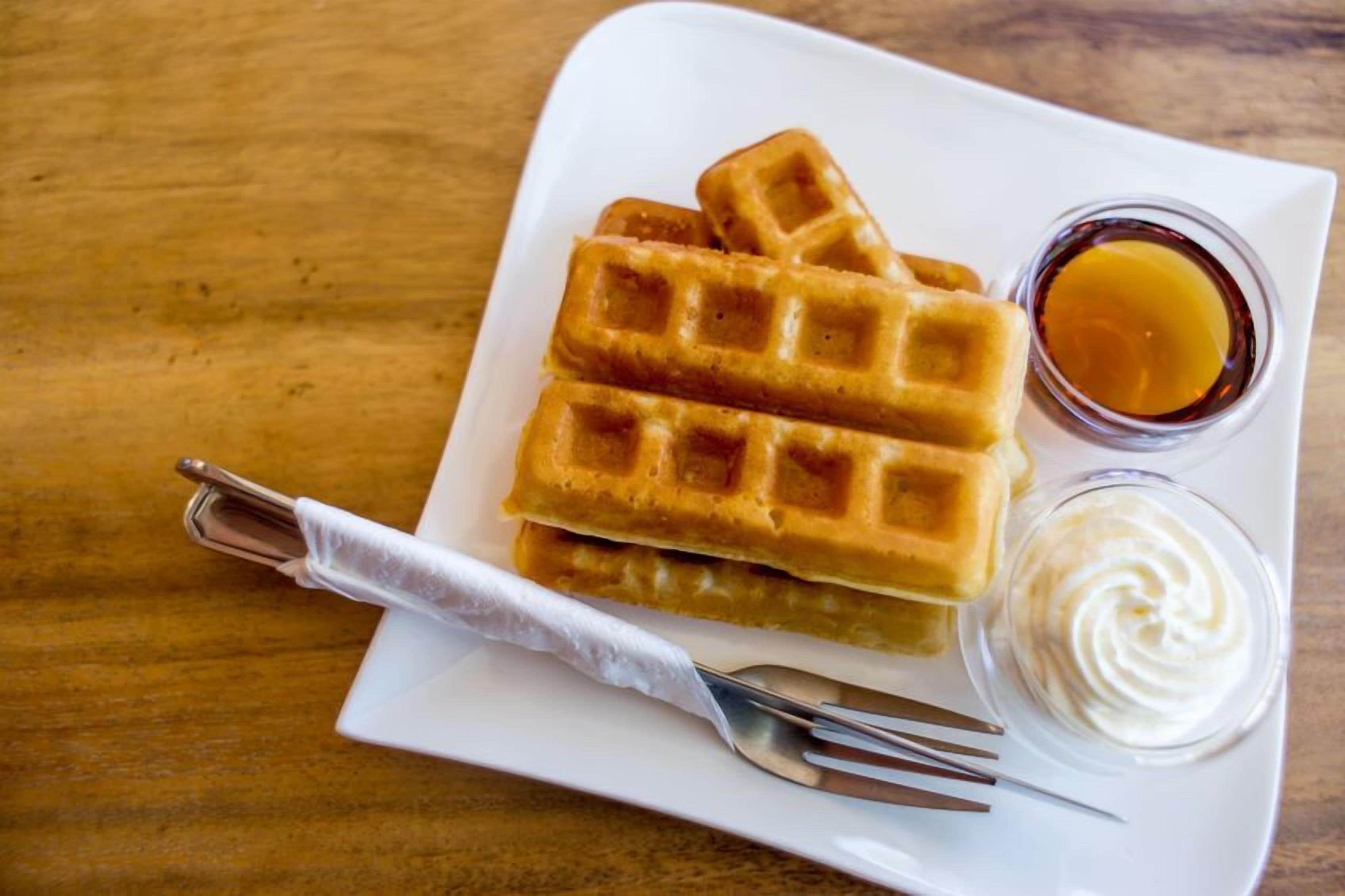 A plate with waffles and two small containers of syrup and whipped cream.