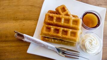 Un plato con waffles y dos recipientes pequeños de jarabe y crema batida.