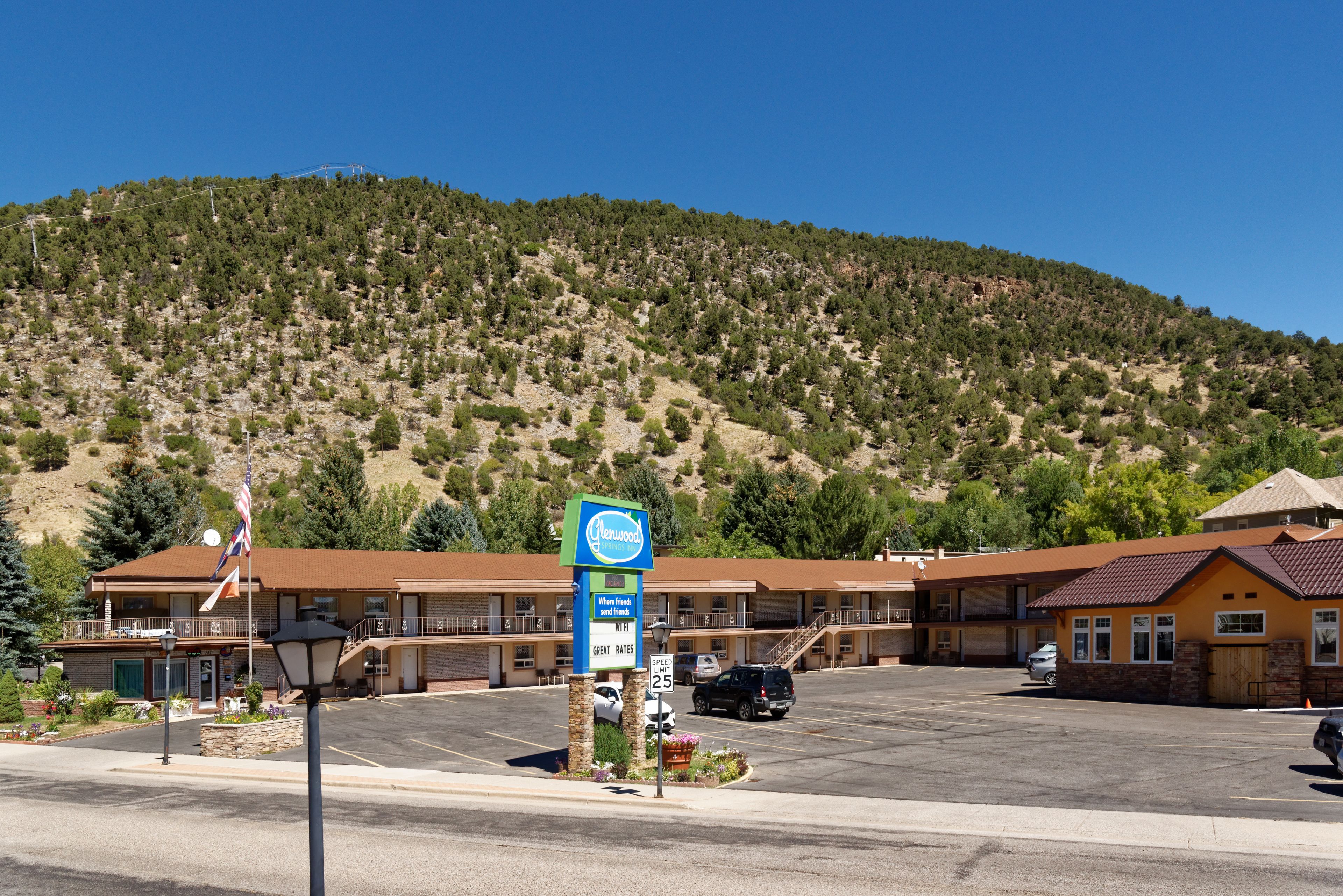 Motel amb un pàrquing, un cartell i un paisatge de muntanyes al fons.
