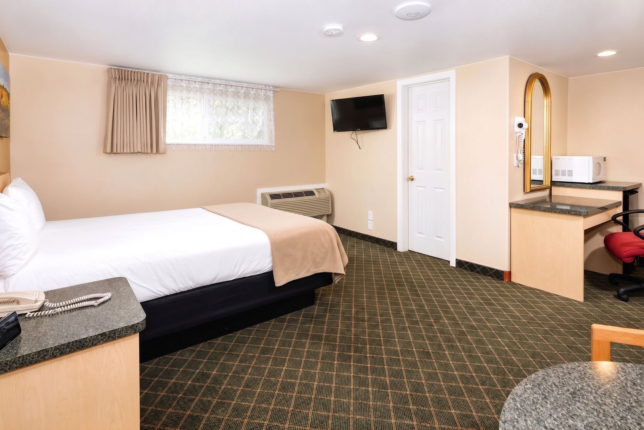 A hotel room with a bed, a desk, a television, and a mirror.