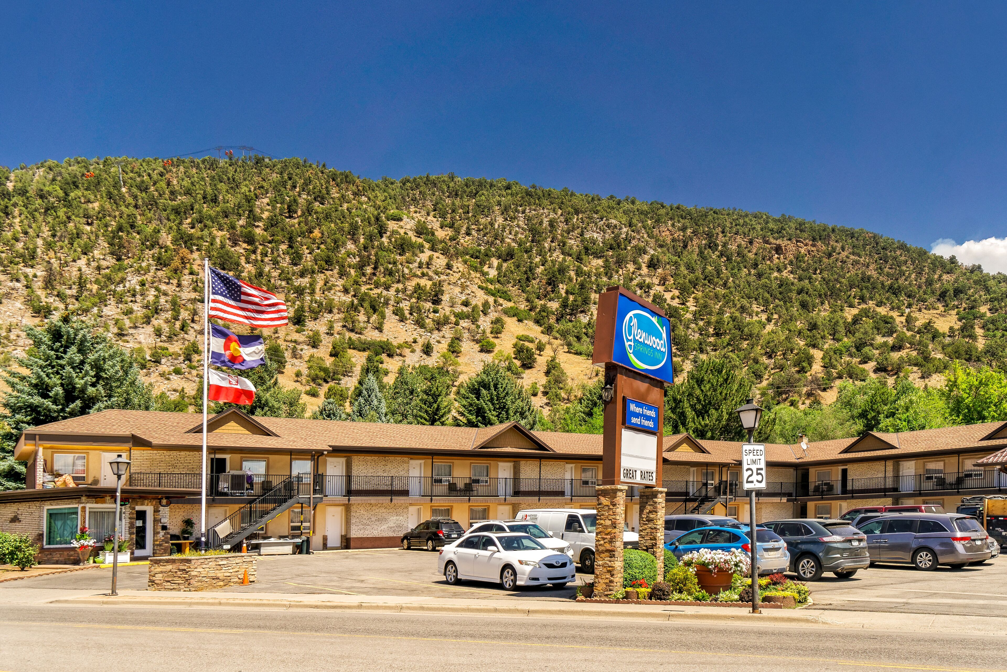 A motel with a mountain backdrop, a speed limit sign, and multiple flags.
