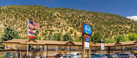 A motel with a mountain backdrop, a speed limit sign, and multiple flags.