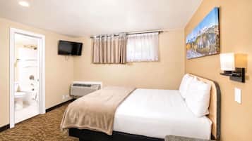 Habitación de hotel con cama, televisión, equipo de aire acondicionado, un cuadro y un baño visible a través de una puerta abierta.