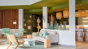 A modern living room with a white sofa, green armchairs, and a wicker chair. There are decorative wall art and a bar area with wicker lamps. - Paradou Mediterranee, BW Signature Collection (Sausset-les-Pins)