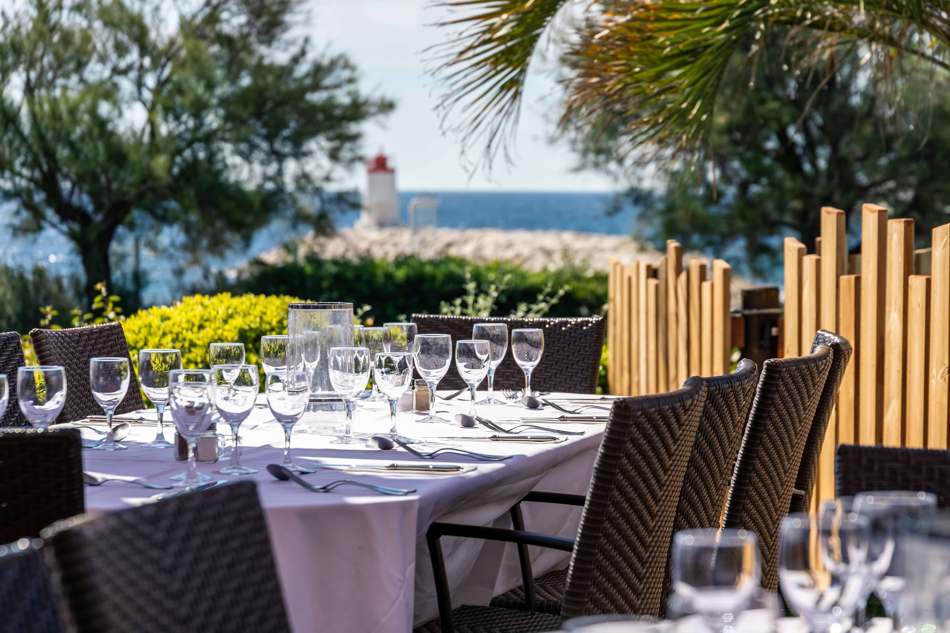 A table set for dining with chairs, a view of the sea, and a lighthouse in the background.