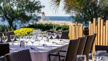 A table set for dining with chairs, a view of the sea, and a lighthouse in the background.