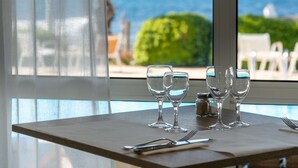 A table with four wine glasses, a fork, and a knife, set against a window overlooking a pool and the sea. - Paradou Mediterranee, BW Signature Collection (Sausset-les-Pins)