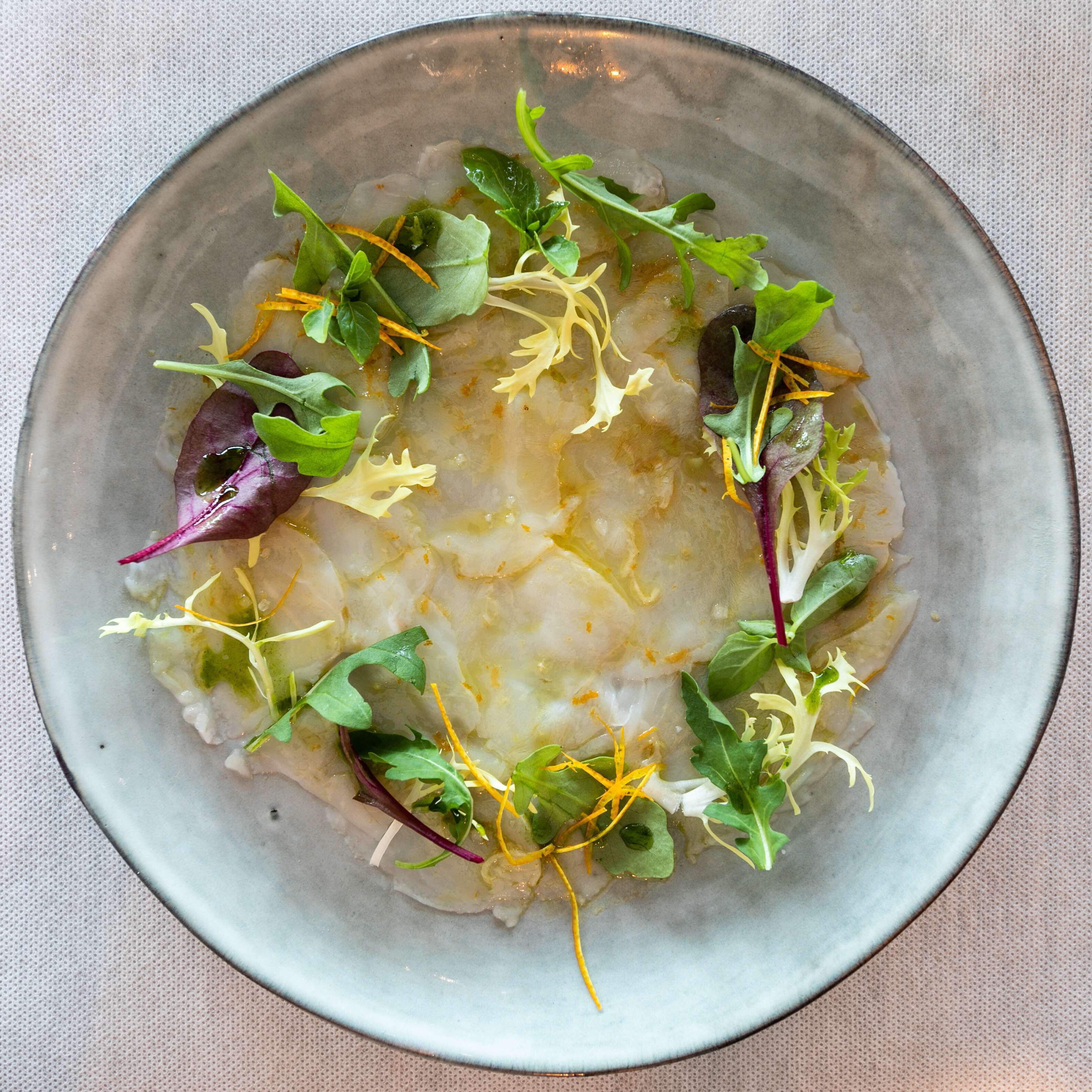 A bowl of food with various greens and thin strips, possibly a salad or appetizer.