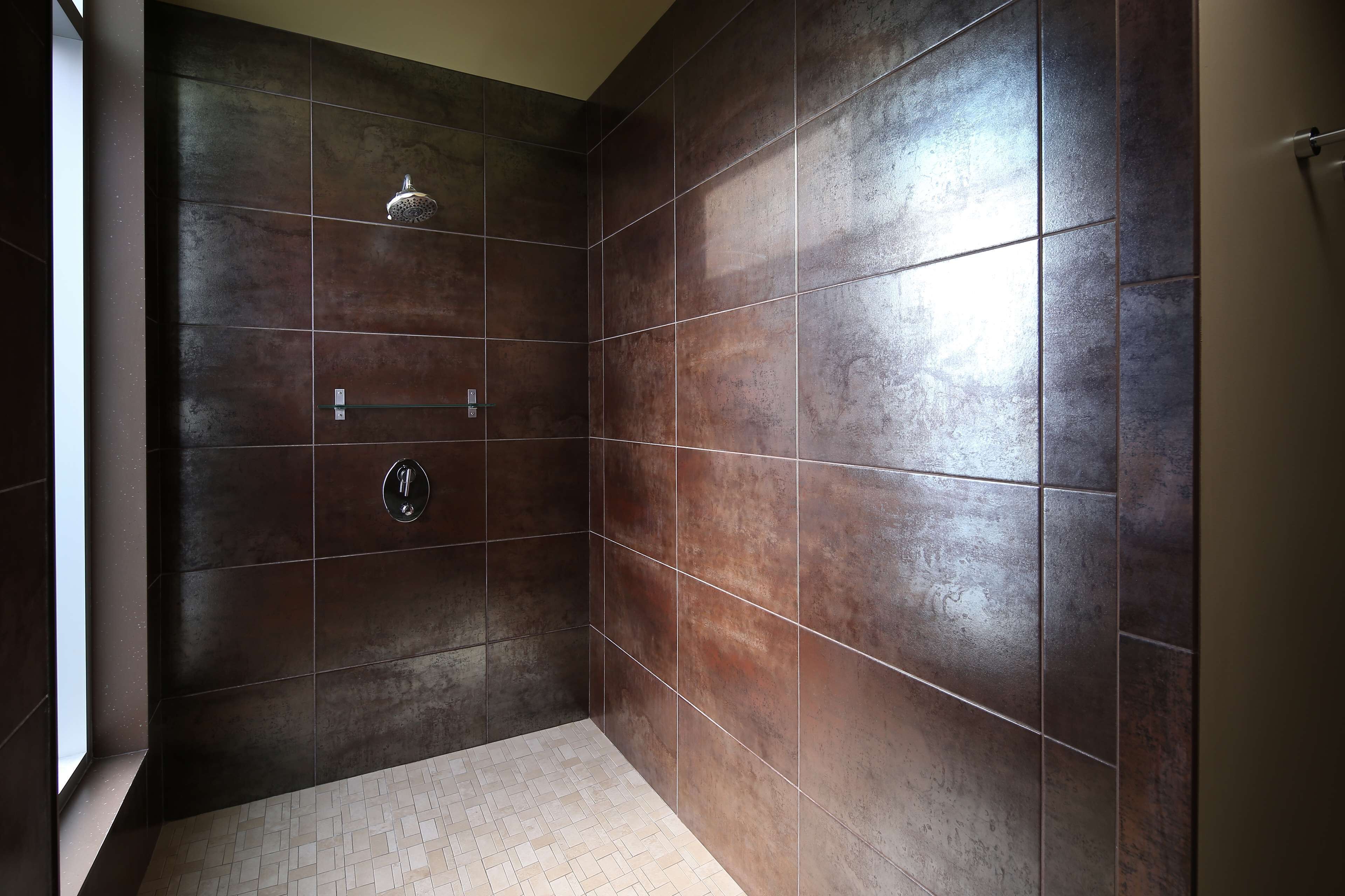 A modern bathroom with dark brown tiles, a shower area, and a tiled floor.