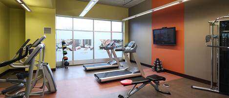 A gym with treadmills, a bench, and a television on the wall.