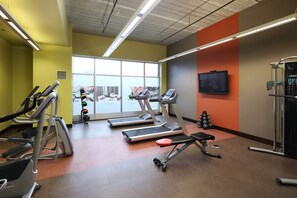 Ein Fitnessraum mit Laufbändern, einer Bank und einem Fernseher an der Wand.