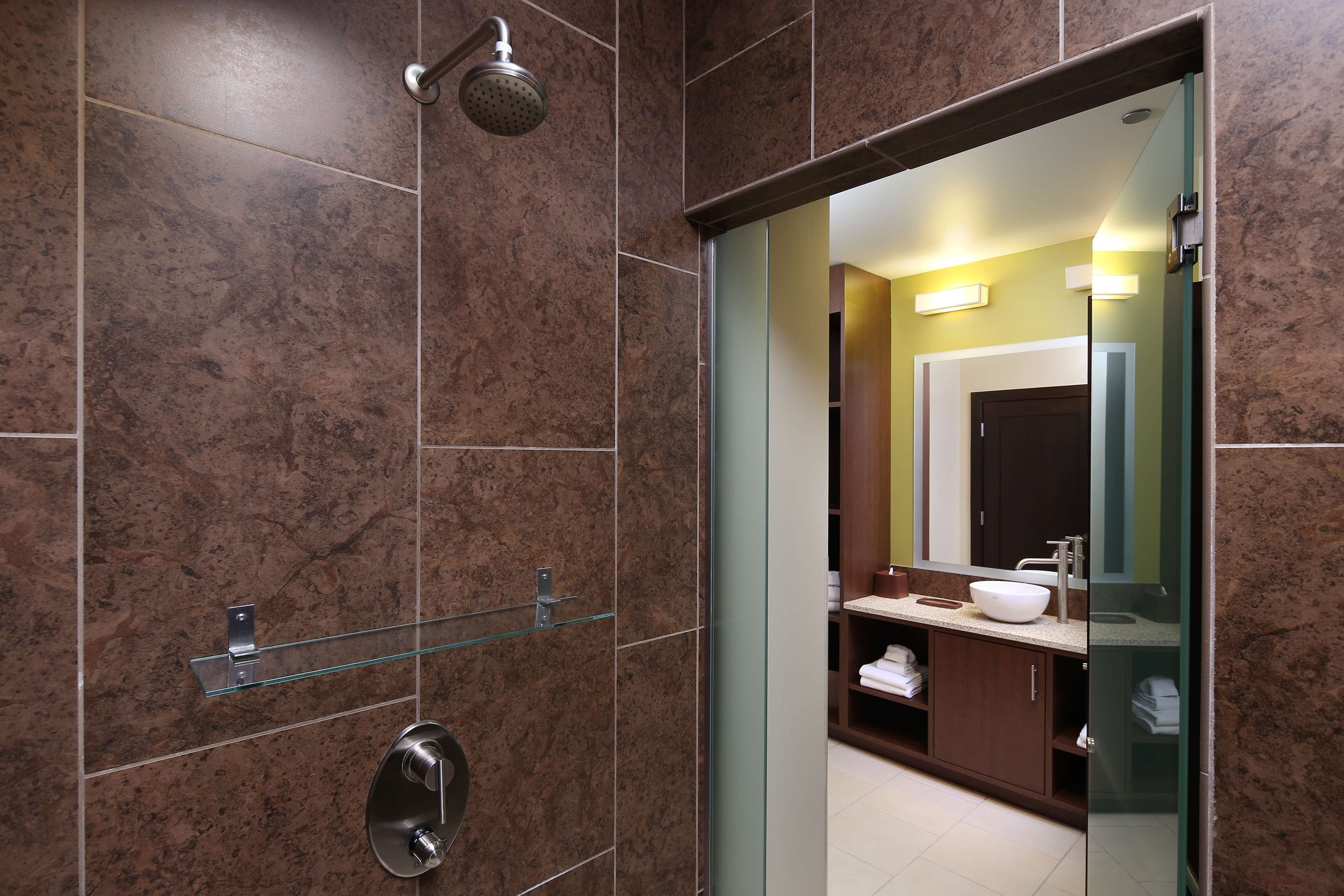 A modern bathroom with a glass shower enclosure, a large mirror, and a vanity with a sink and towel storage.