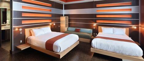 A modern hotel room with two beds, a sofa, and built-in shelving with integrated lighting.