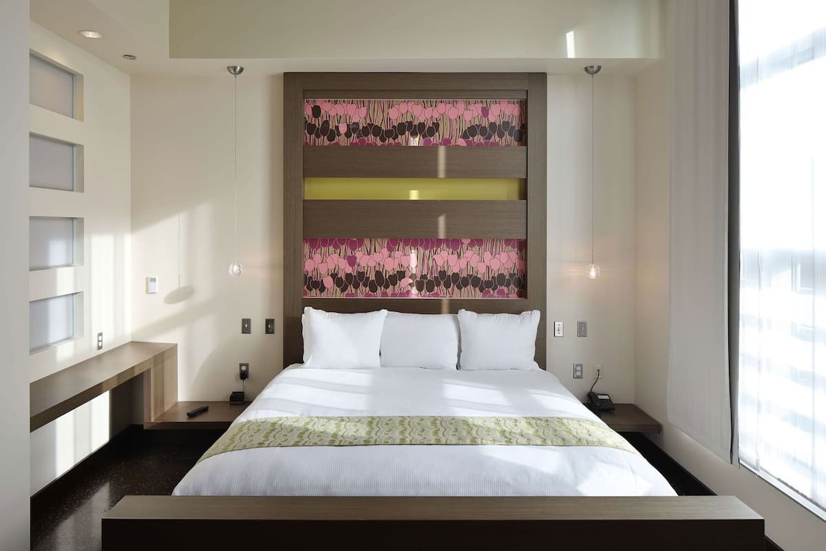 Een moderne hotelkamer met een groot bed, een hoofdbord met bloemenprint, inbouwkasten, nachtkastjes en een groot raam.
