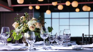 Een gedekte tafel voor een formele diners met een bloemstuk als middelpunt, glazen servies en een moderne kroonluchter op de achtergrond.