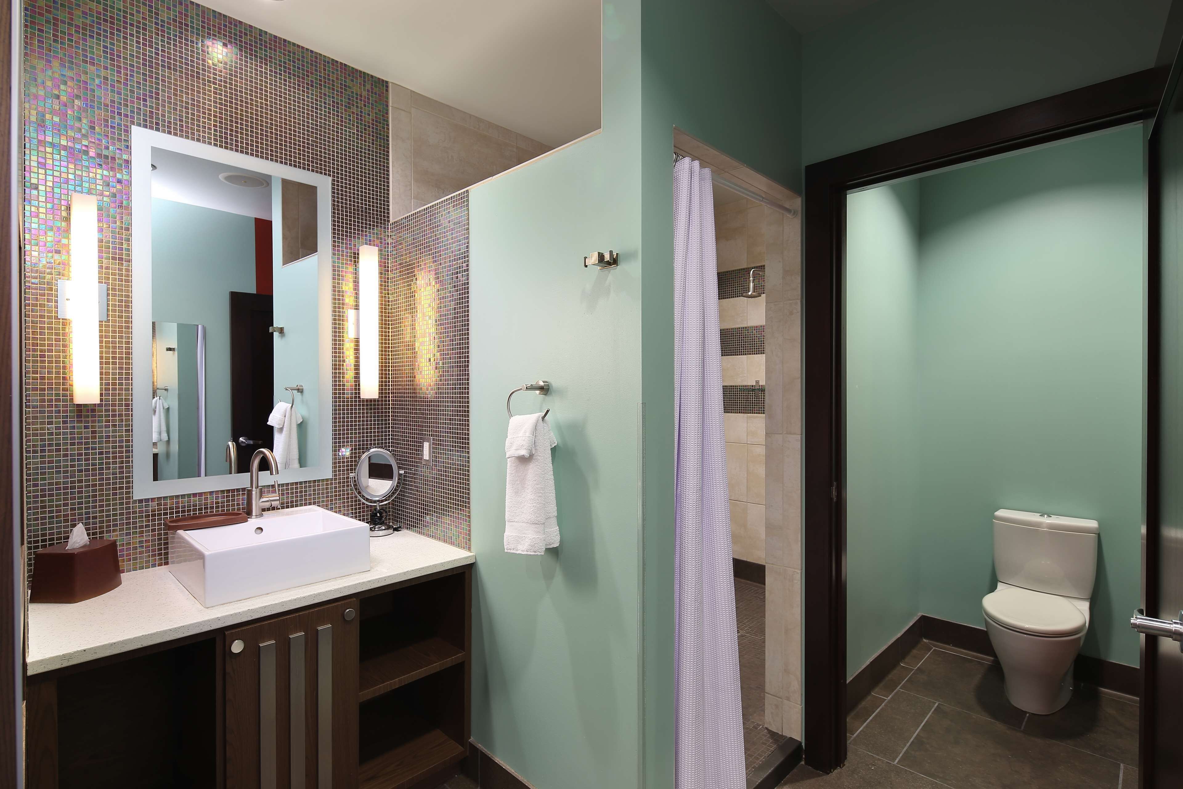 A modern bathroom with a large mirror, a sink, a toilet, and a shower area.