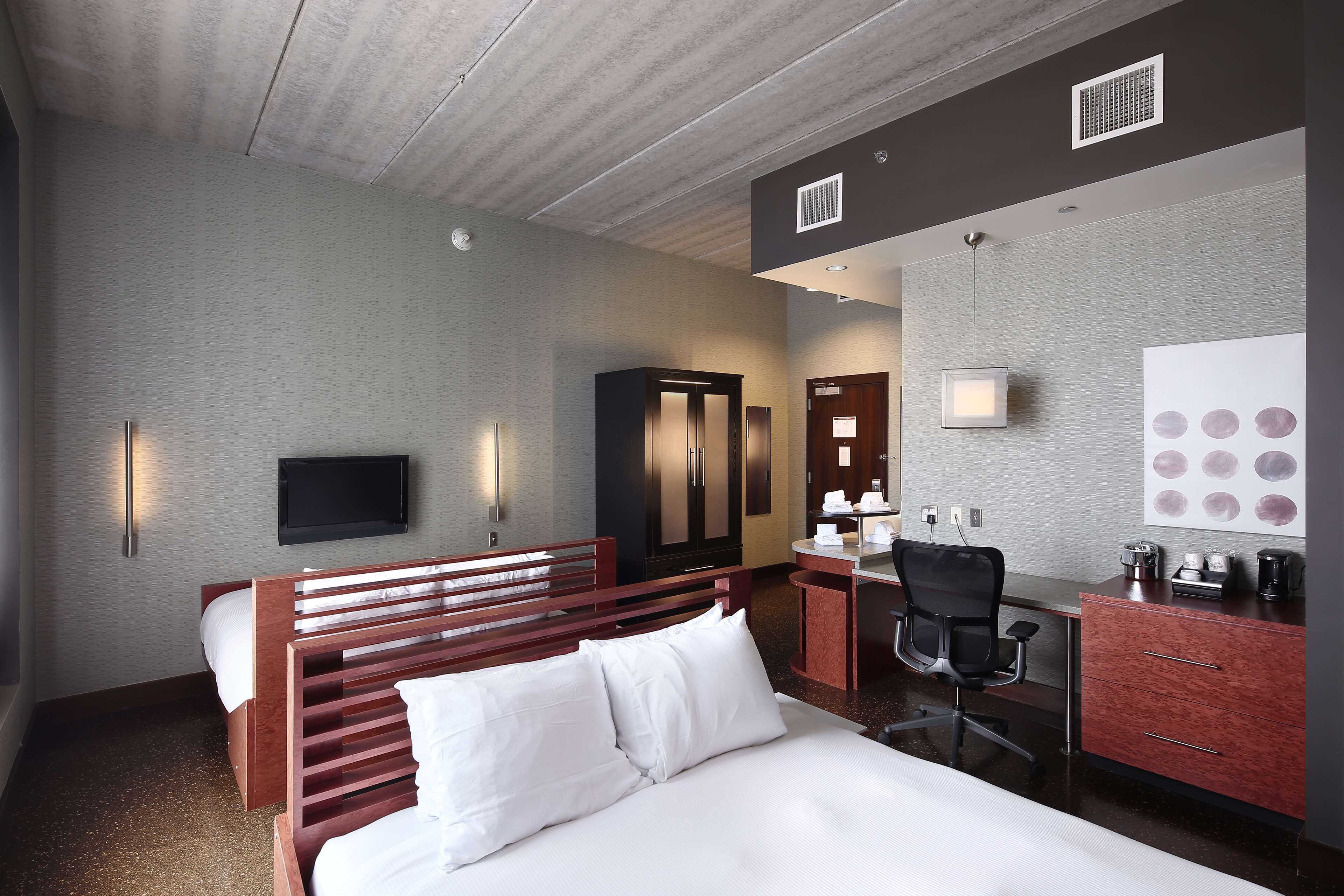 A hotel room with a bed, a desk, a chair, a wardrobe, a television, and a wall with circular decorations.