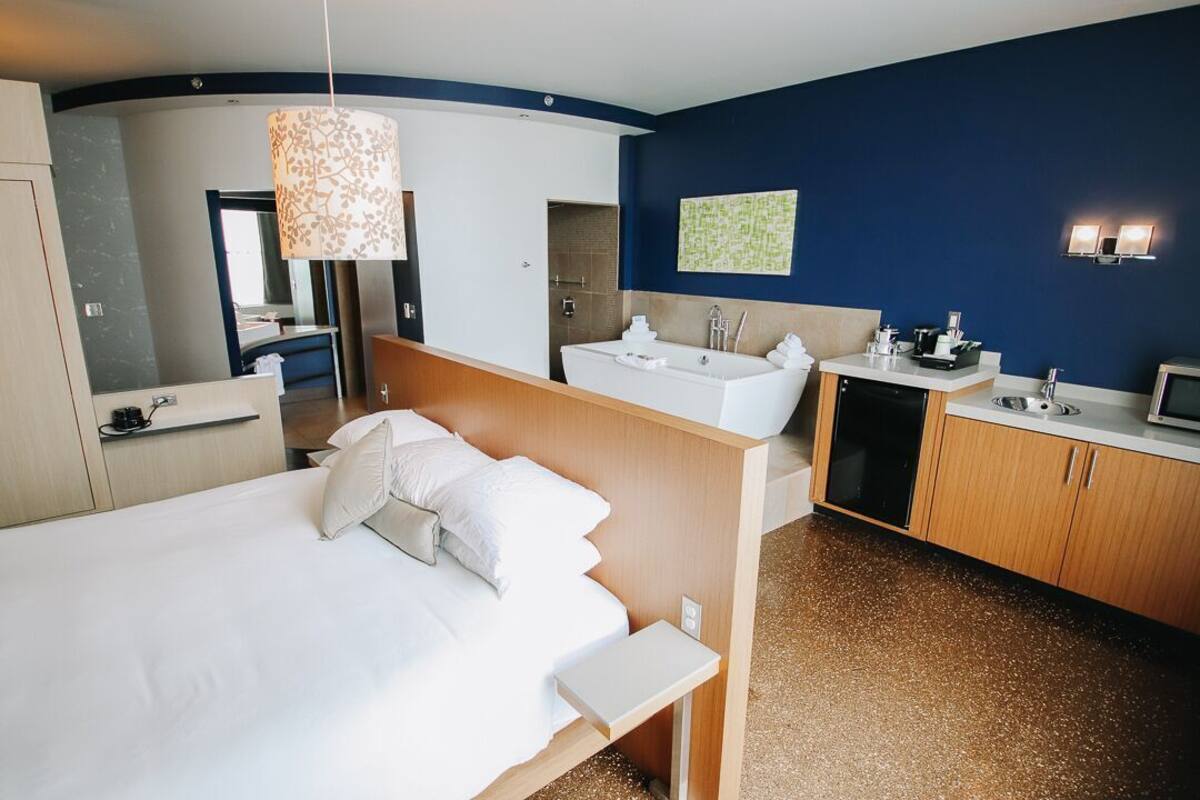 Een moderne hotelkamer met een bed, een badkamer met een badkuip, een wastafel en een kleine kitchenette.